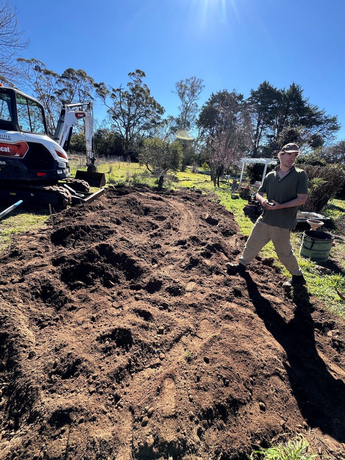 Fresh soil piled for garden beds, a small excavator and Finley in the background.