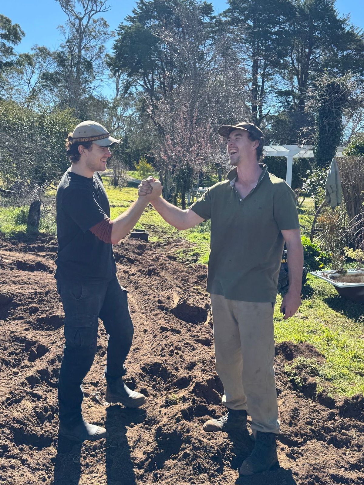 Finley and George shaking hands on a freshly dug garden bed.
