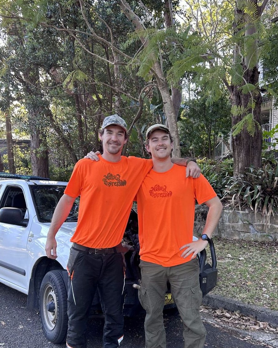 Finley and George in Natural Progression shirts in front of the ute, under gum trees.